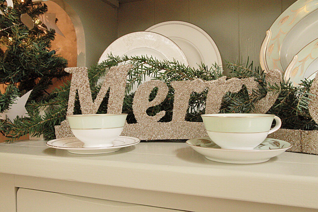 A Merry sign on the counter behind tea cups.