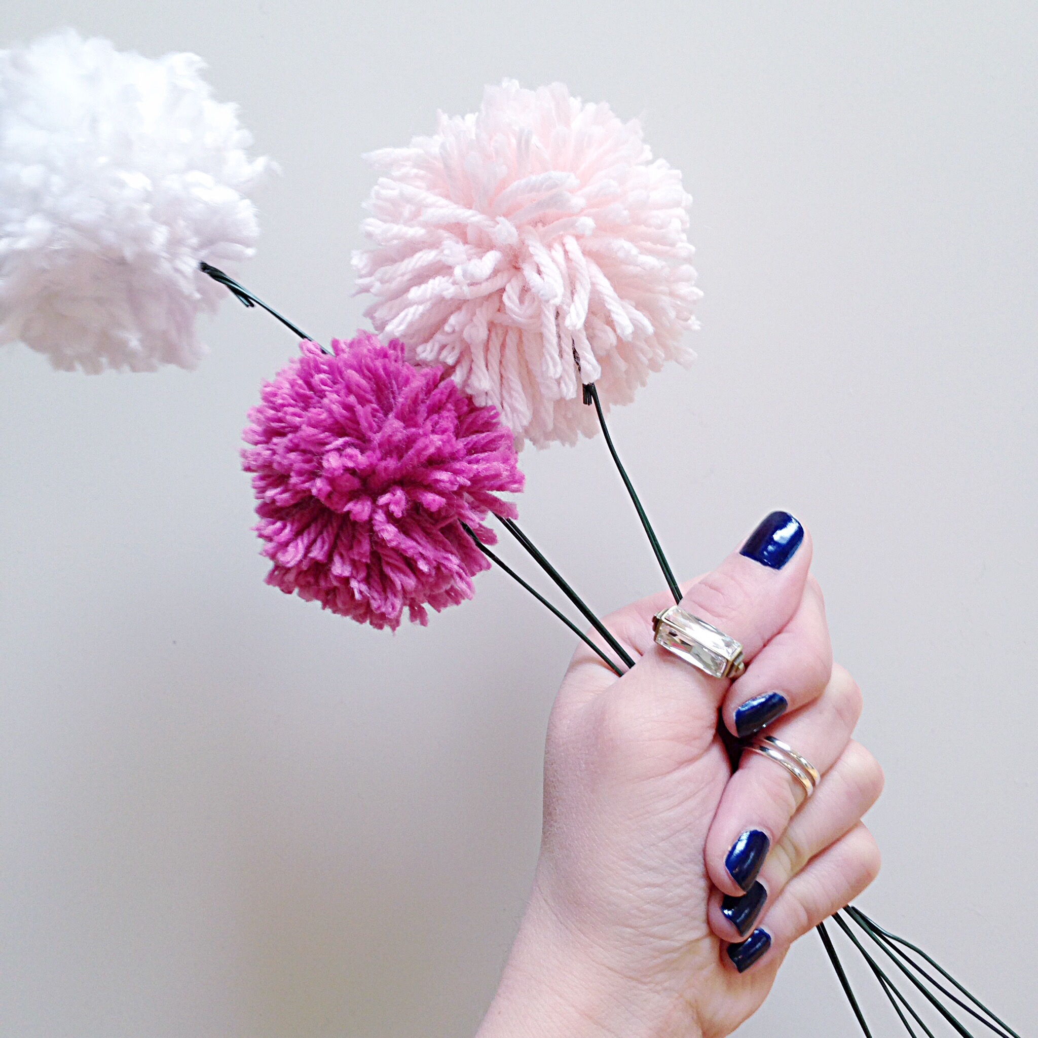 The Pom Pom flowers in a persons hand who has blue nail polish.