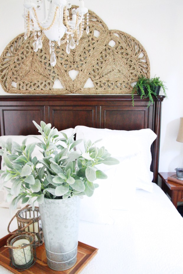 A woven rug above the headboard, a chandelier and a tray with candles and a plant on it.