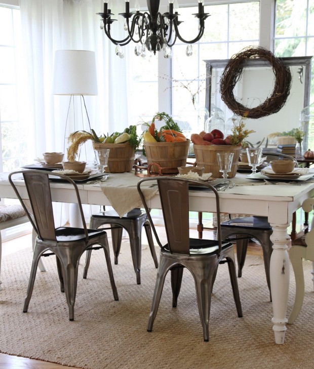 Dining room decorated for Thanksgiving with a wreath by the window, wooden buckets full of vegetables and pumpkins on the table.