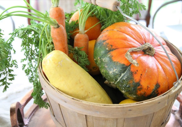 A wooden bucket with pumpkins, potatoes and carrrots.