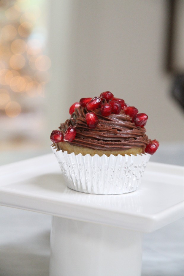 A white muffin covered in chocolate icing and pomegranates on top.