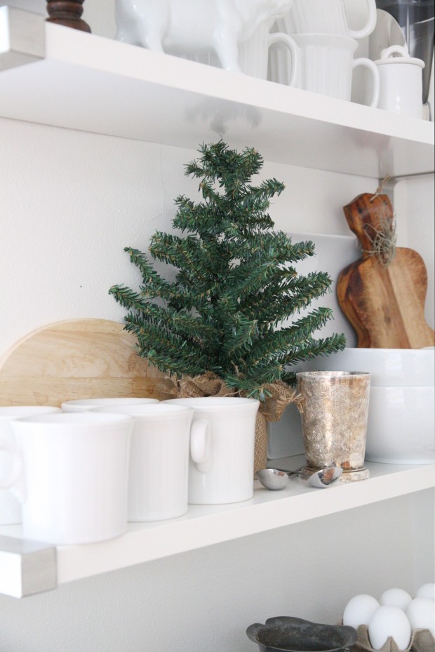 A mini evergreen tree on the open shelf in the kitchen.