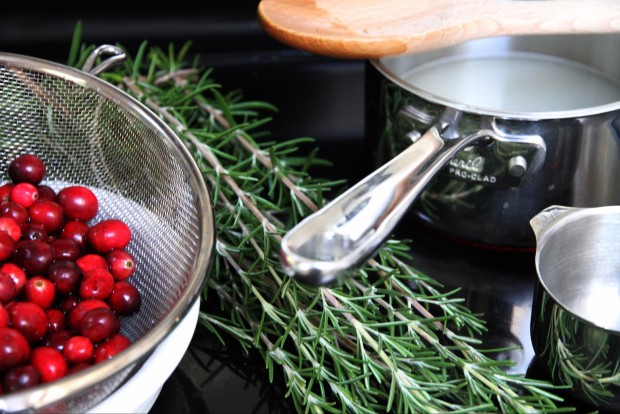 Cranberries in a strainer, and rosemary on the counter.