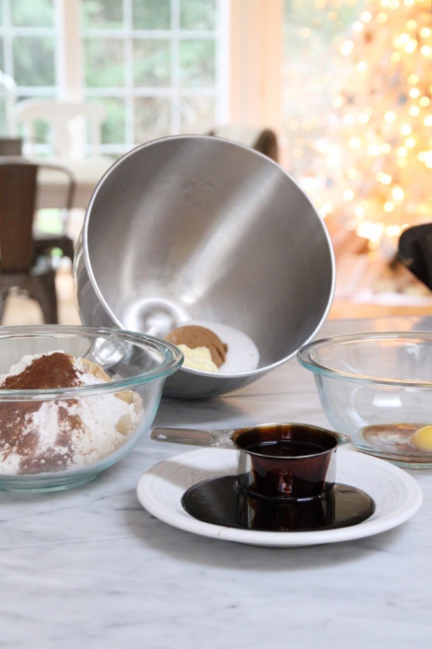 A steel mixing bowl lying on its side, a measuring cup with molasses and a clear bowl with a flour mixture inside it.