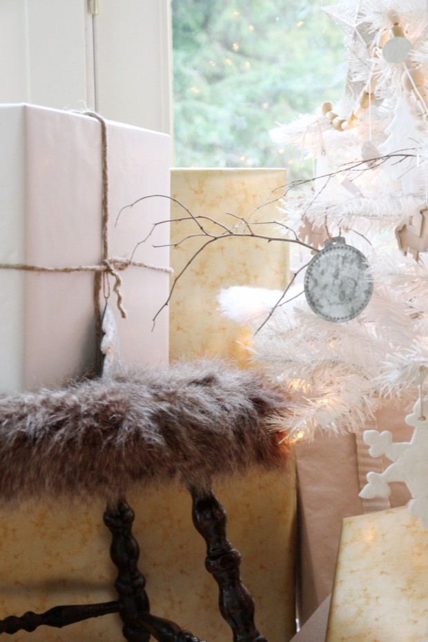 A wooden stool with a faux fur top beside the presents under the white tree.
