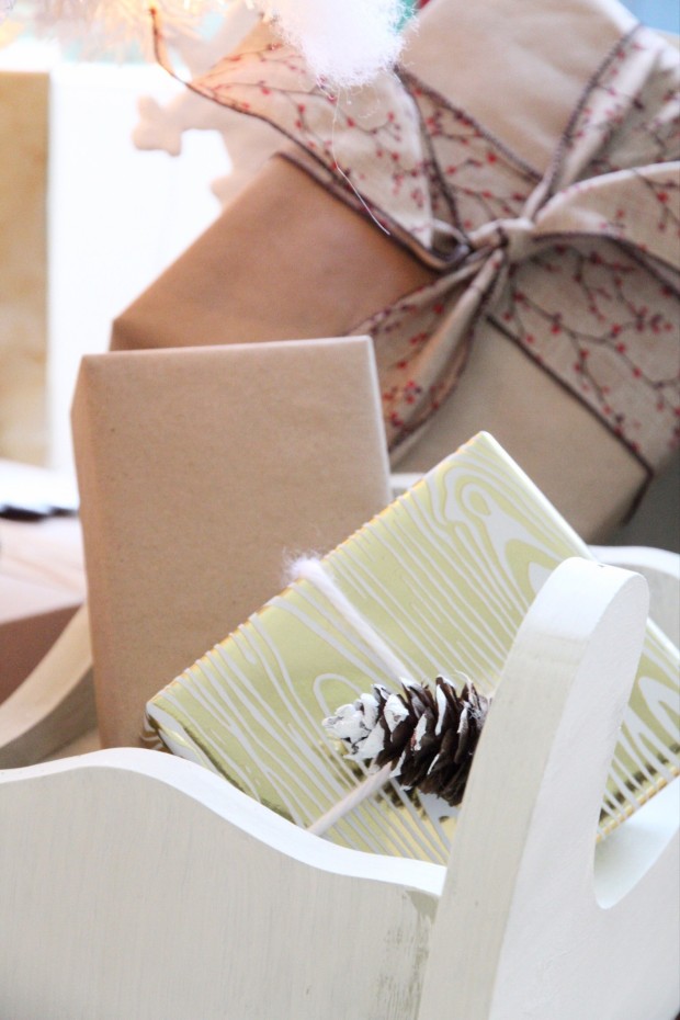 A present wrapped in light green and white with a pine cone on it under the tree.