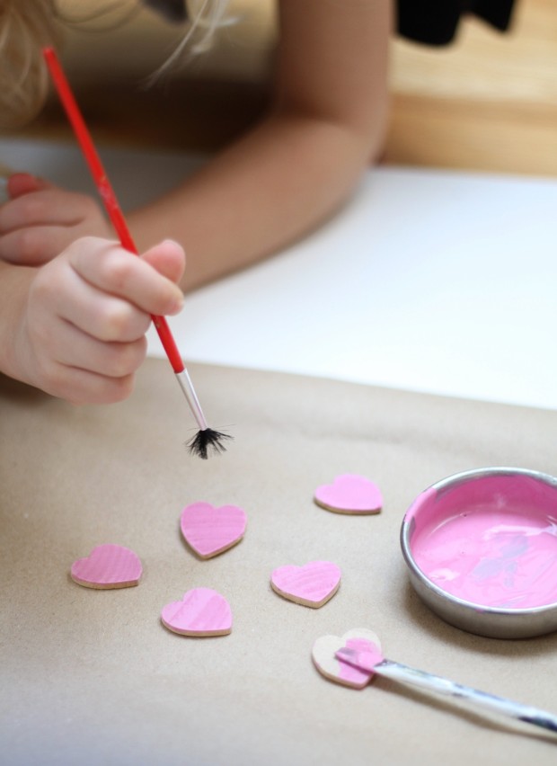 Pink paint in a small container and children painting the heart pieces.