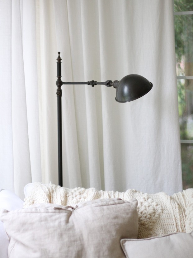 A brushed bronze antique stand up lamp behind the white couch.