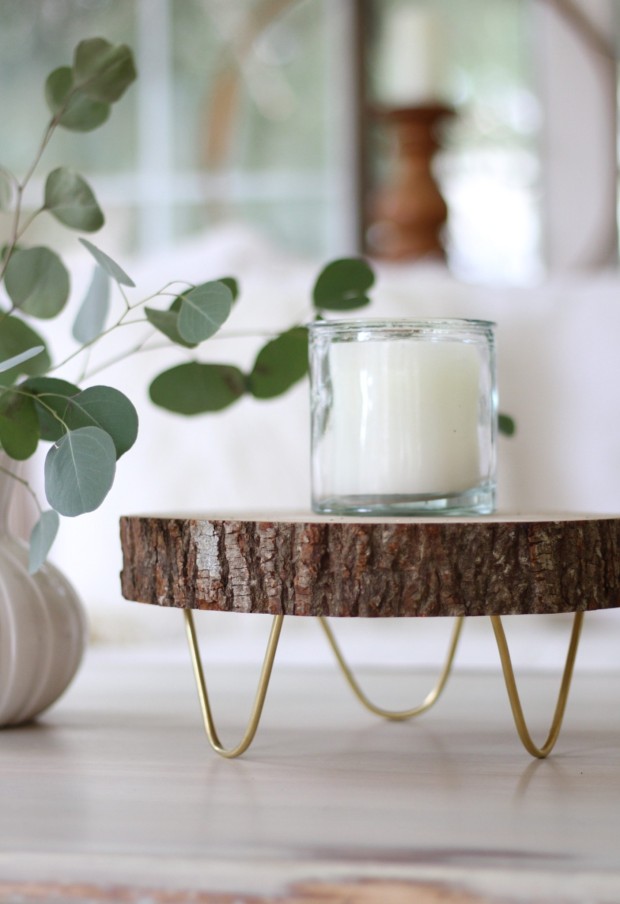 A white candle in a glass jar on the wooden circular tray.