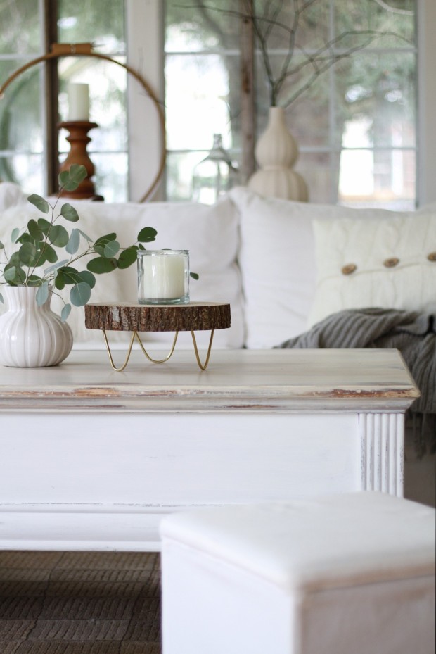 A round wooden tray in a white living room with eucapyptus plant in a vase beside it.