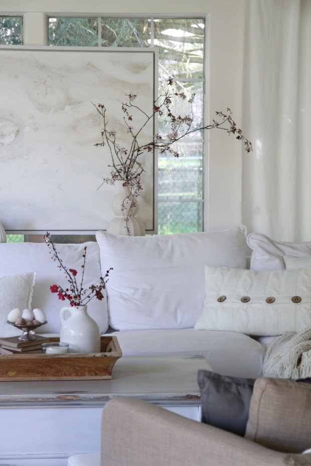 The white sofa, with a coffee table in the middle of the room and a vase on the table.