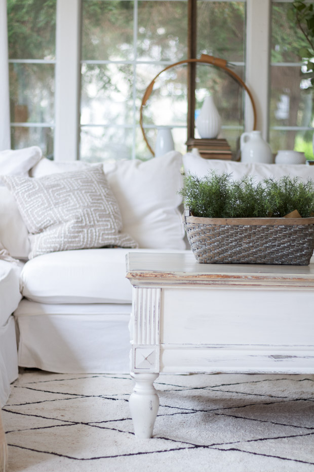 White couch with white wooden table and greenery in a basket on it.