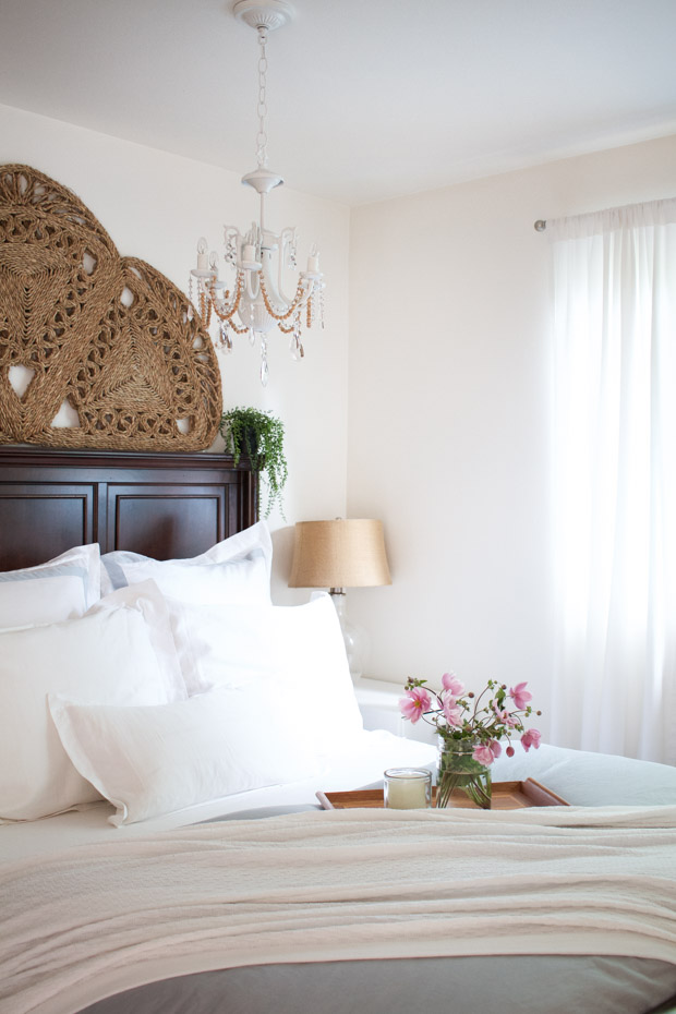 Large bed with white linens and a tray with a vase and pink flowers on it.