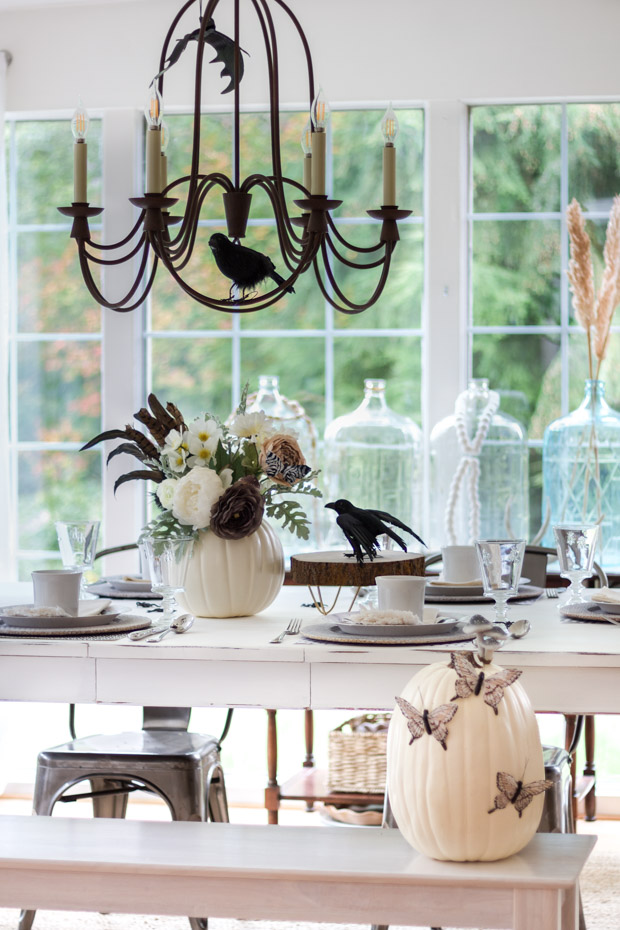 White, brown and green floral arrangement, black crow all on dining table.