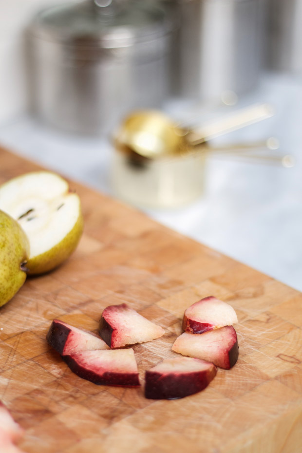 Plums cut into quarters on a cutting board with half a pear in the background.