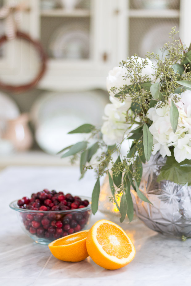 An orange cut in half and cranberries in a bowl on the counter.