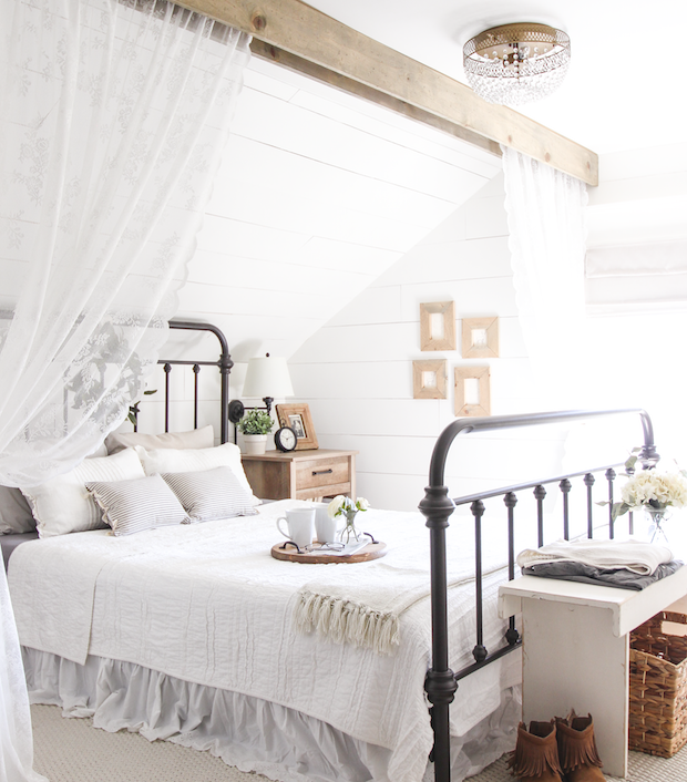 A wrought iron bed, with white linen and a wooden beam above it.