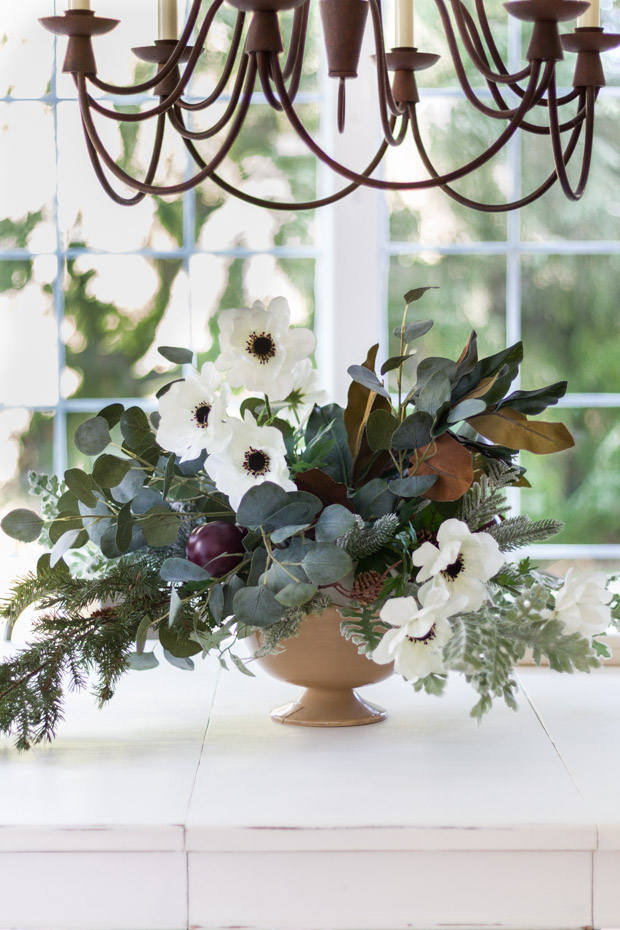 The floral arrangement on the table underneath a metal chandelier.