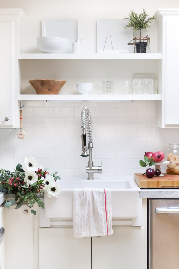 The kitchen sink, with open shelves above the sink and flowers beside it lying on the counter.