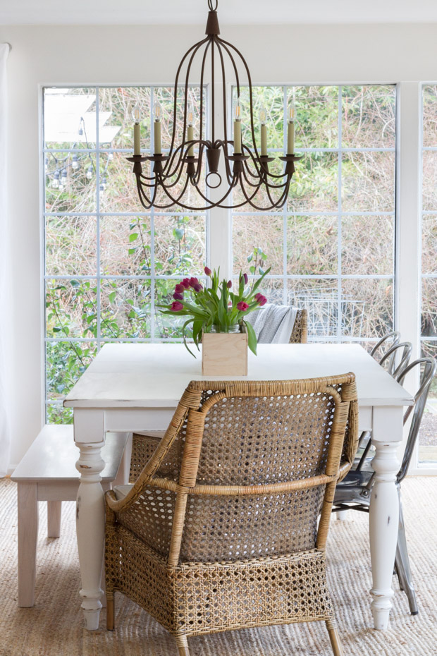 The dining room table with a wicker chair and a wrought iron chandelier.