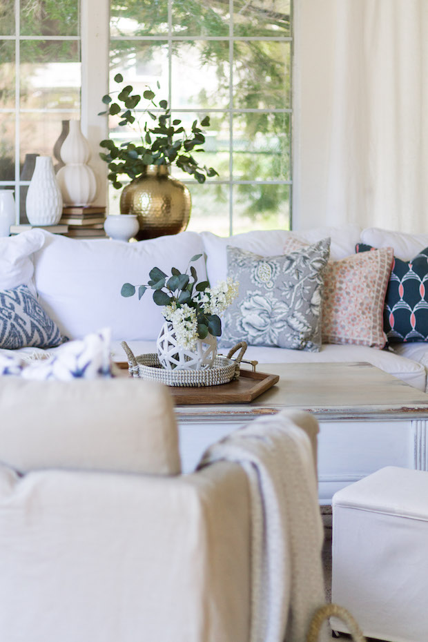 A pretty white vase in the living room with greenery in it surrounded by neutral couches.