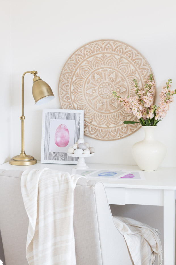 A white desk with a white blanket hanging on the back of the chair and the Easter egg printable on the desk.