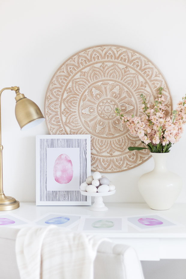 The framed printable on the desk beside the white vase and a large picture on the wall.