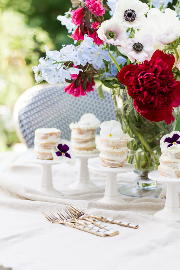 Little mini naked cakes on individual stands with red, white and pink flowers in a vase beside them.