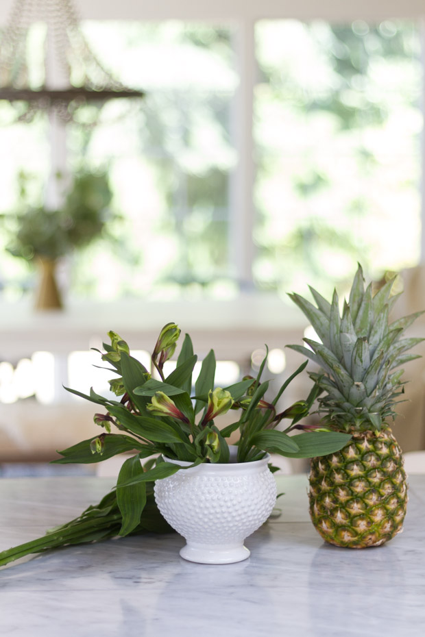 Pineapple sitting on counter with vase full of greenery.