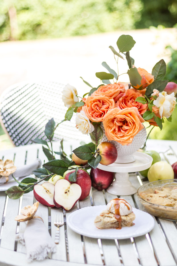 Flowers and apples with pie on plate on table.