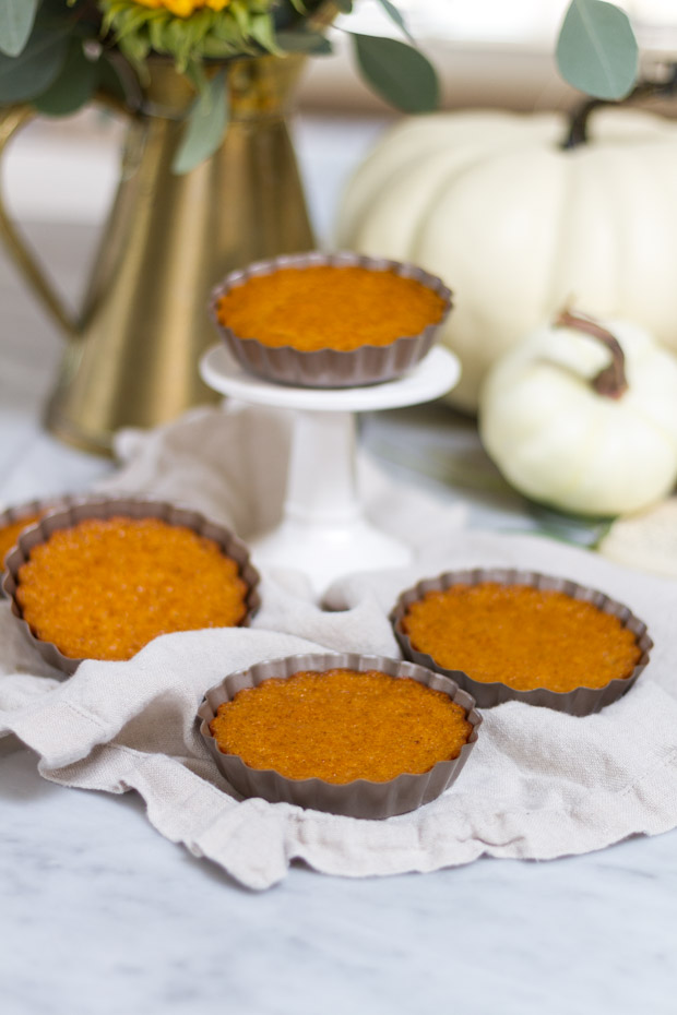 Pumpkin mini tarts on the counter and one on a small cake pedestal.