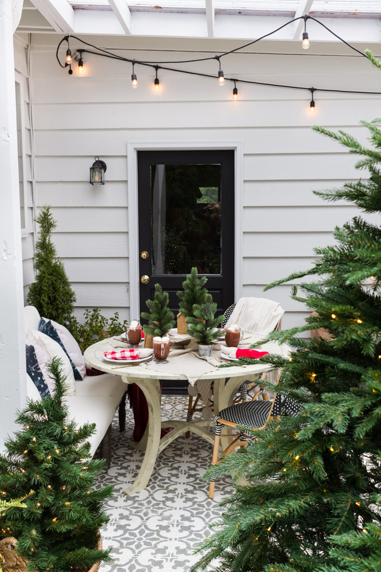 The simple outdoor table surrounded by evergreen trees and a string of lights on the patio.