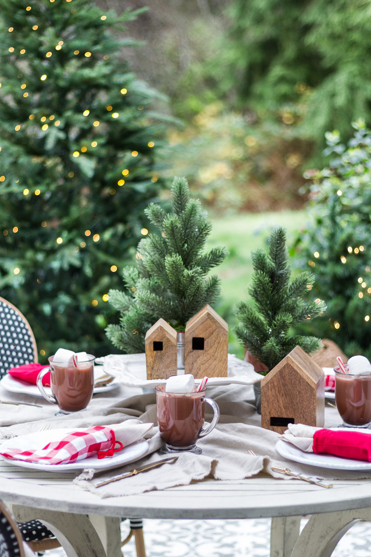 A round outdoor table, hot chocolate, birdhouses, and stocking napkin holders on the table.