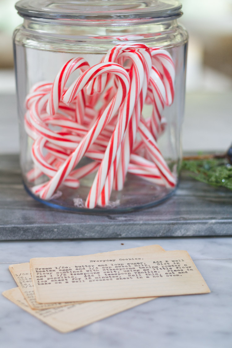 A jar full of candy canes and recipe cards in front of it.