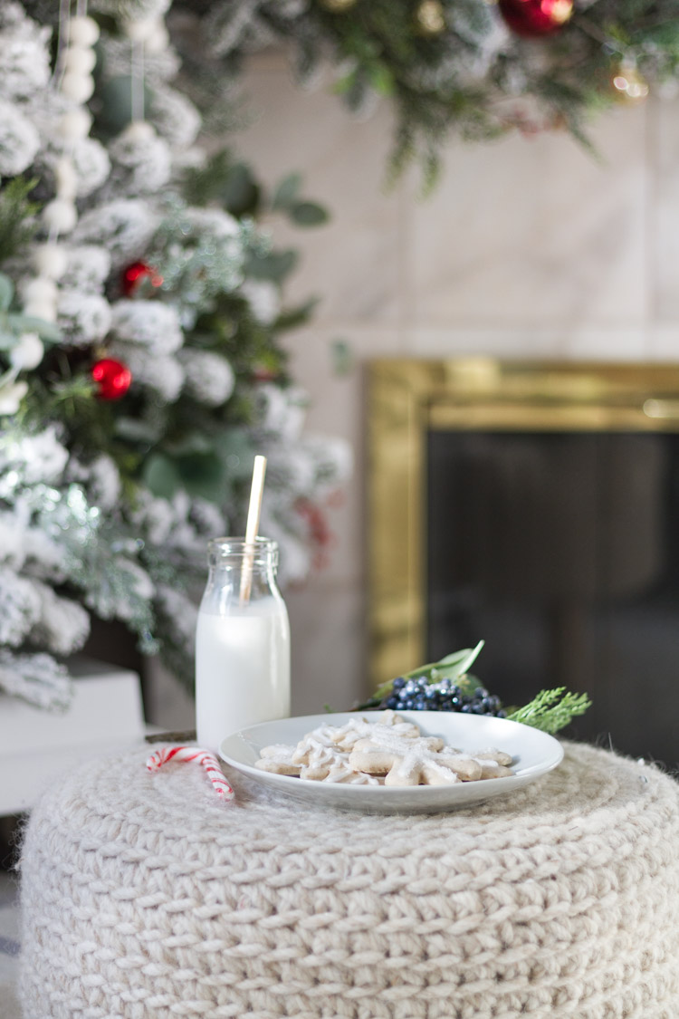 The sugar cookies, a glass of milk with a straw in it, and a candy cane on a small stool beside the tree.
