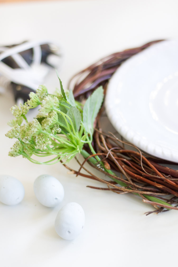 The grapevine wreath underneath a white plate and a sprig of greenery beside it.