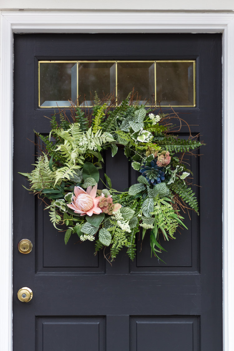 A dark gray door with a fresh whimsical spring wreath on the door.