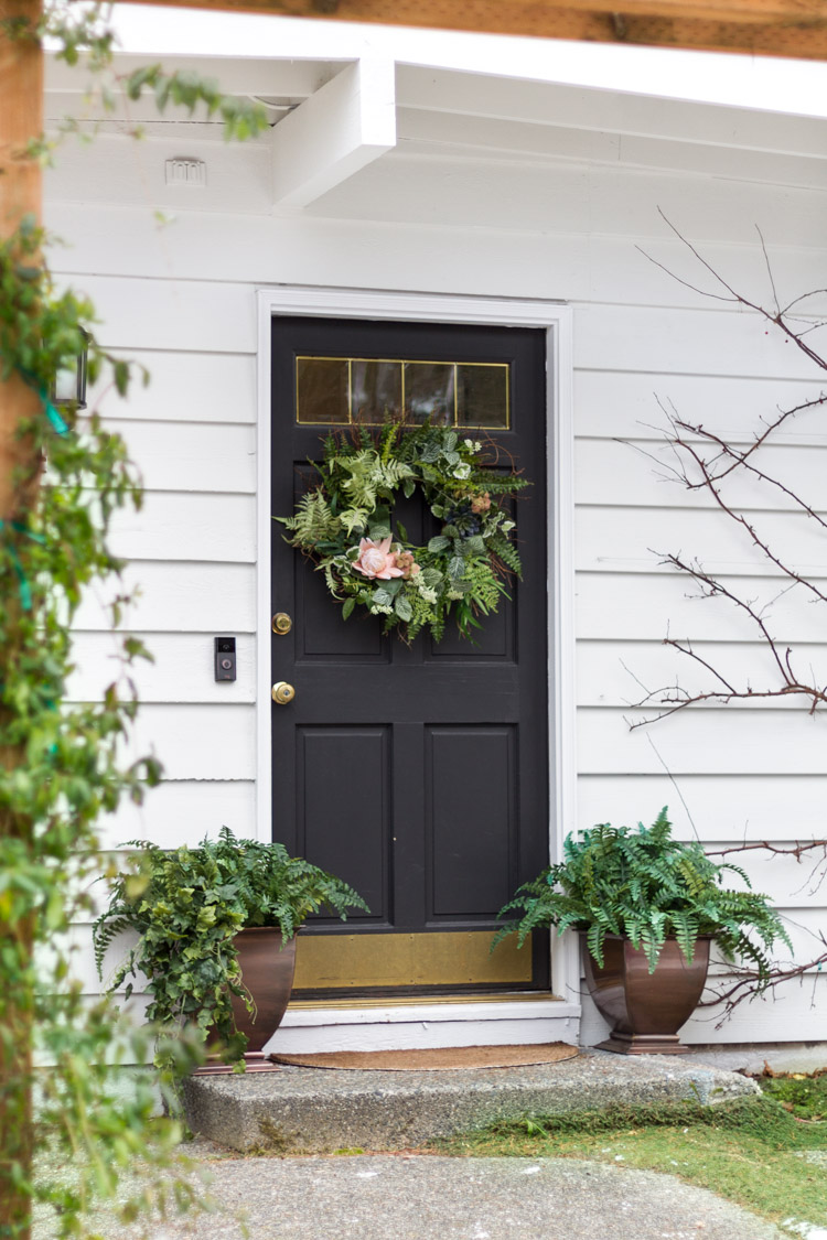 The front porch of a house with a whimsical wreath on the door.