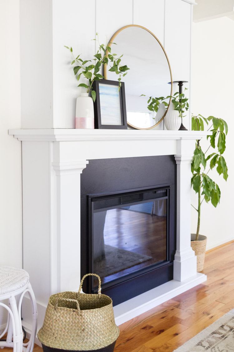 A large round mirror on the mantel with vases and plants beside it.