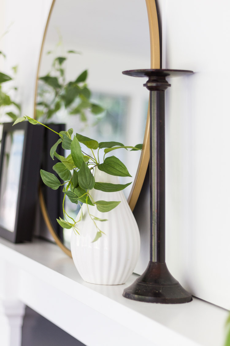 A white vase, a candlestick, mirror and picture on the white mantel.