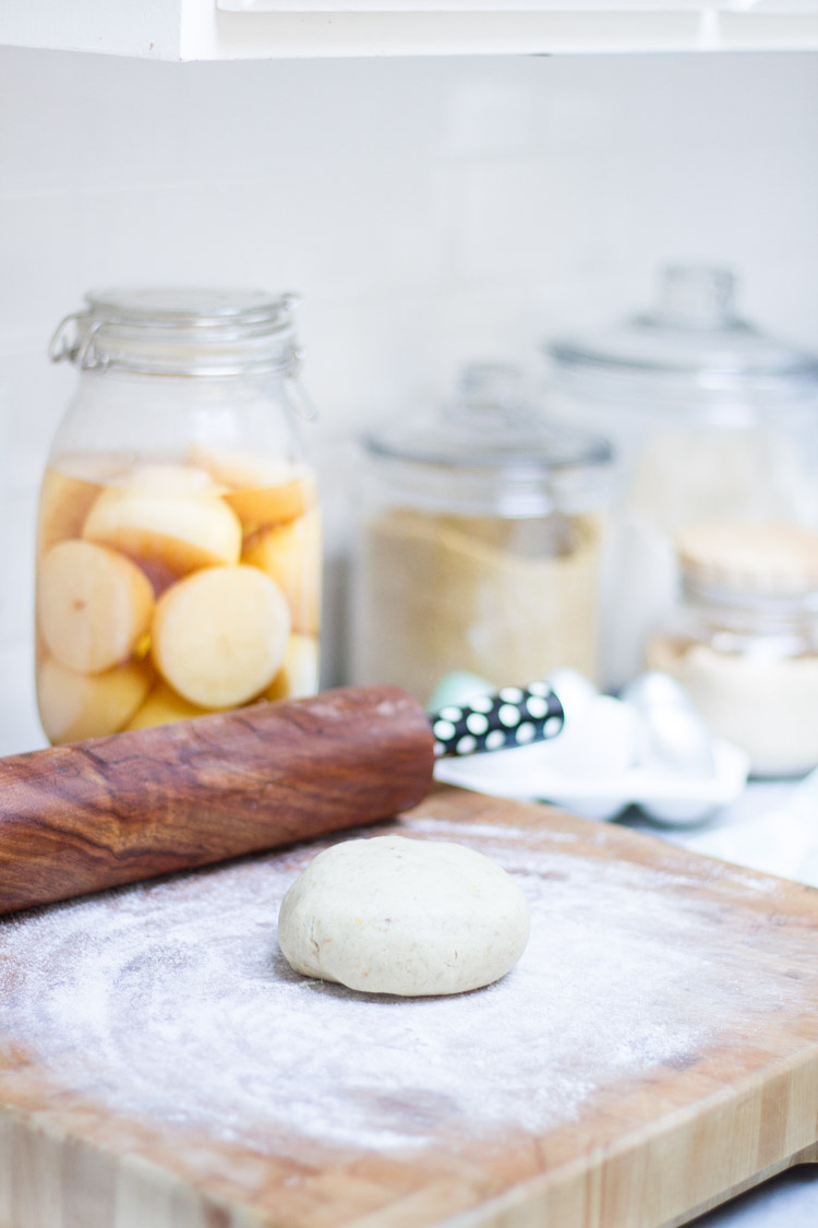 The sugar cookie dough on a wooden cutting board with a rolling pin beside it.