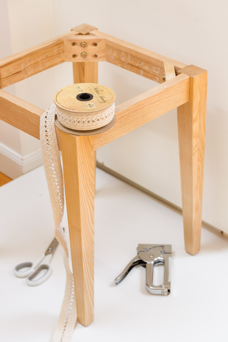 The wooden legs of the side table with a spool of ribbon on it.