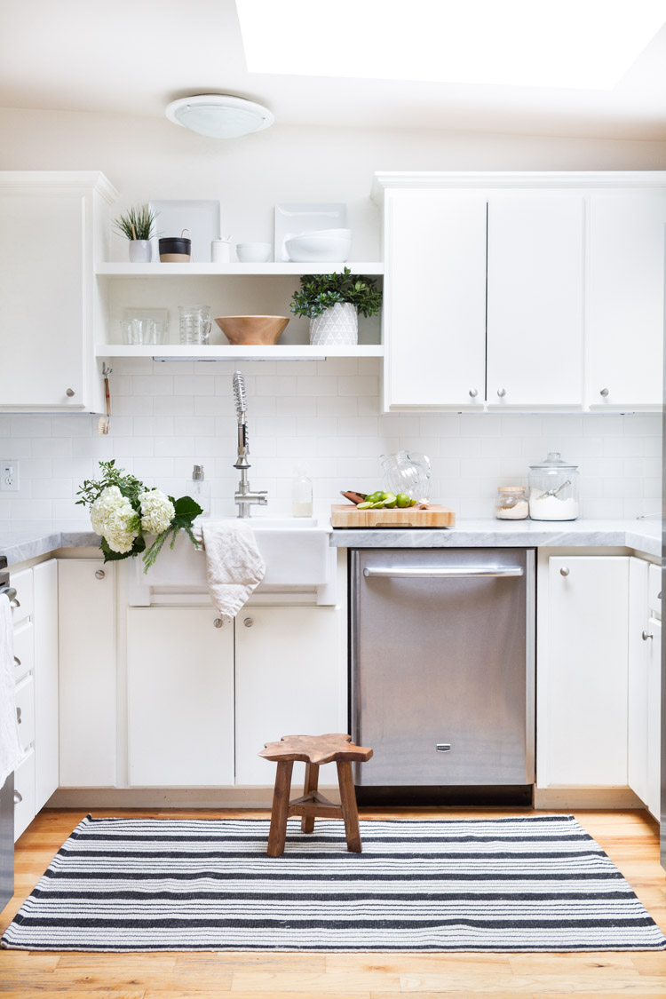 White kitchen with blue striped rug and foot stool.