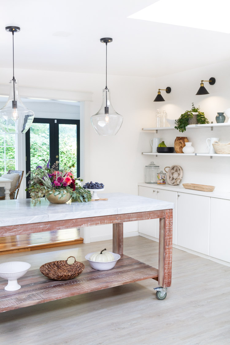 A white and wood island in kitchen that is on wheels.