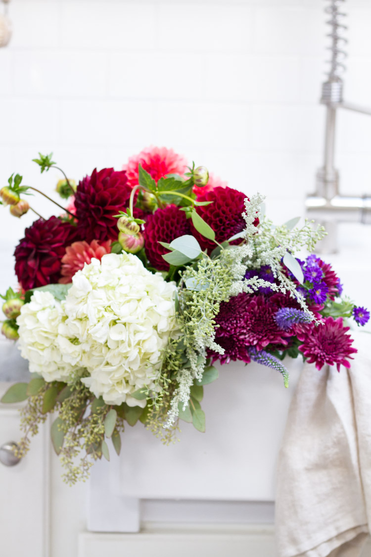 White, red, purple, pink and green flowers in a bouquet lying by the farmhouse sink.