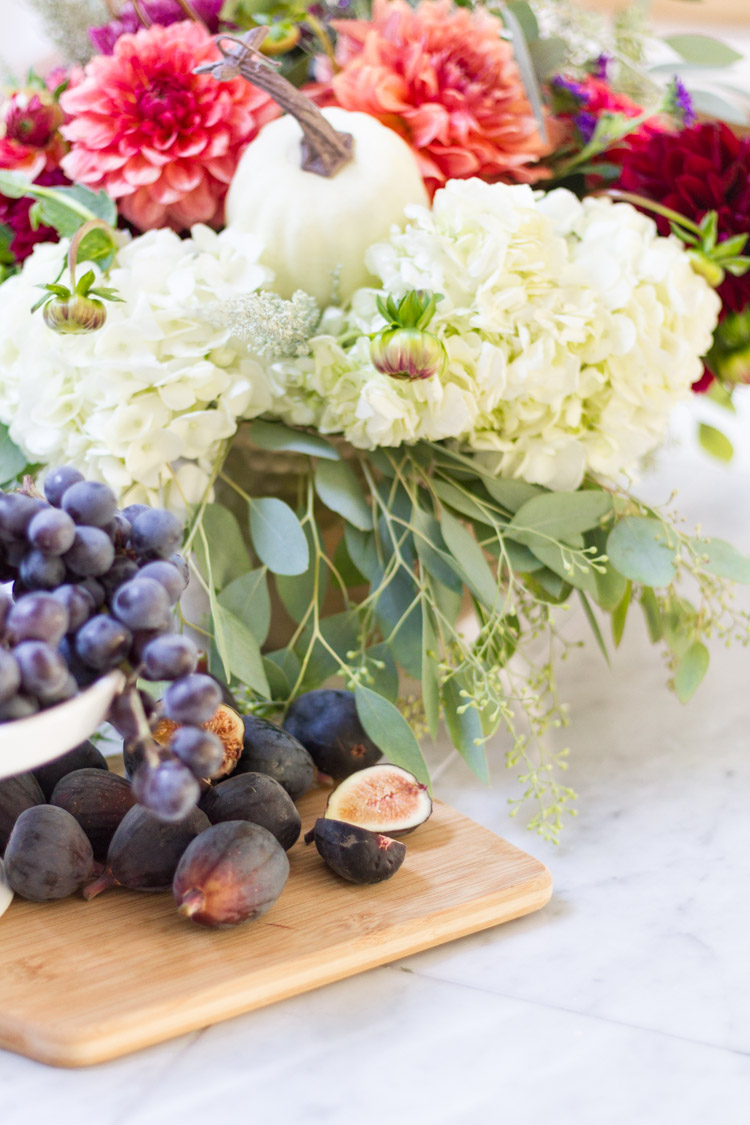 Figs, grapes and flowers in kitchen on marble counter.