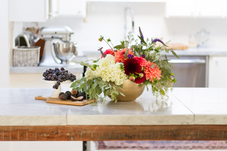 A brass vase filled with flowers and a bowl full of grapes on the counter in kitchen.
