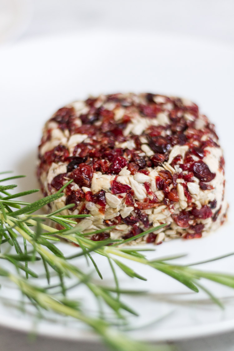 Up close picture of the vegan Cranberry Cheese Loaf with a sprig of greenery on a white plate.
