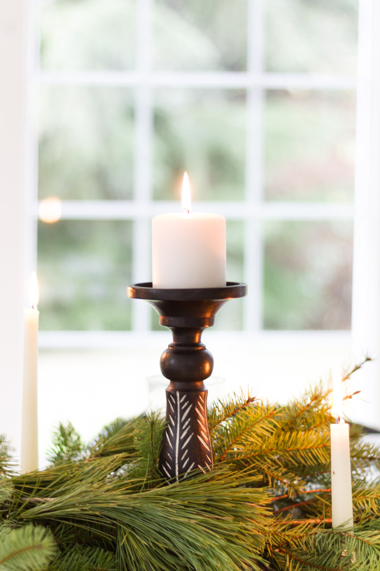 A single candle surrounded by branches of a pine tree on the table.